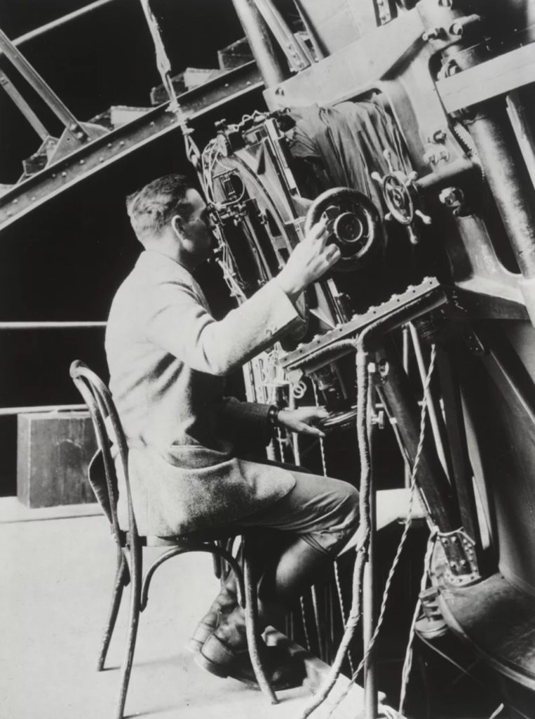 Edwin Powell Hubble seated at the Newtonian focus of the 100-inch reflecting telescope, Mount Wilson Observatory.
