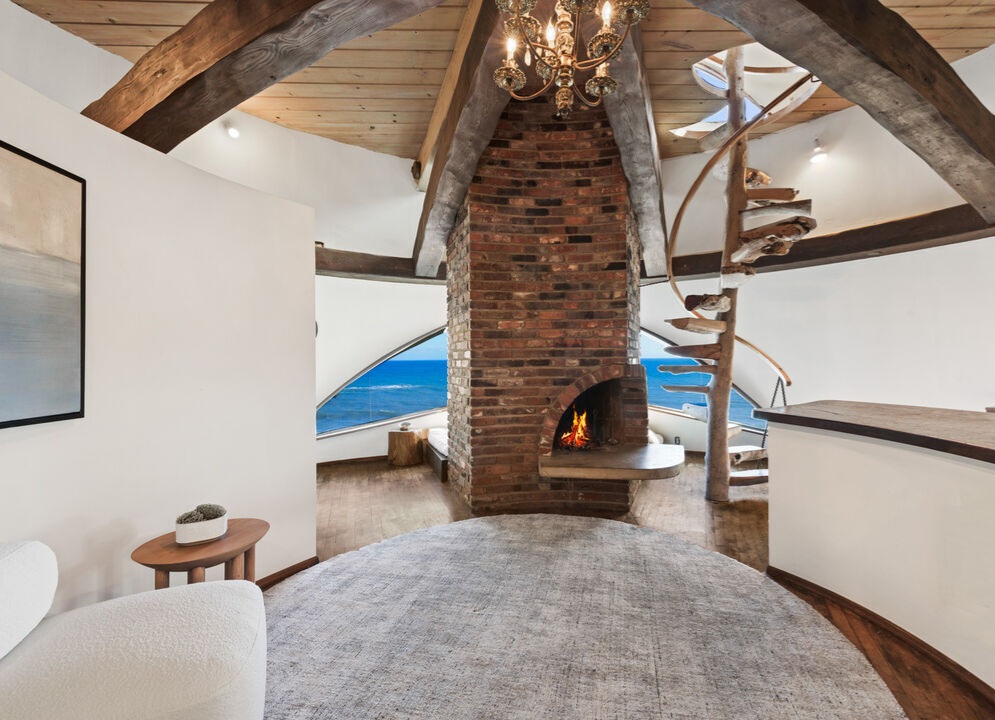 Harry Gesner’s Malibu Sandcastle Upstairs is the primary suite tower, with high ceilings, huge beams, charming eyebrow windows, a brick fireplace, an ocean-view sitting area, and a spiral staircase with handmade driftwood treads leading up to a studio/loft/meditation space.